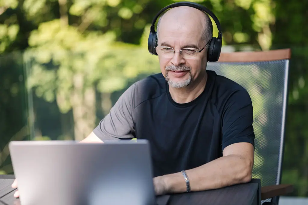 Mann mit Kopfhörern sitzt an einem Tisch vor einem Laptop im Freien